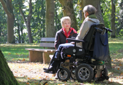 Hospizhelferin unterhält sich mit Dame im Rollstuhl